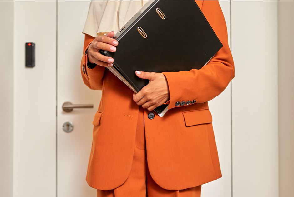 Entretien annuel 2026 : 4 heures pour négocier son salaire A close-up of a female office worker holding a file folder while standing in front of a closed door.