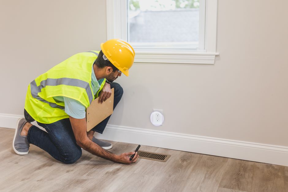 Frais de télétravail : 3 dépenses à vérifier sur la paie A construction worker in a hard hat inspects a floor vent indoors, ensuring quality and safety standards.