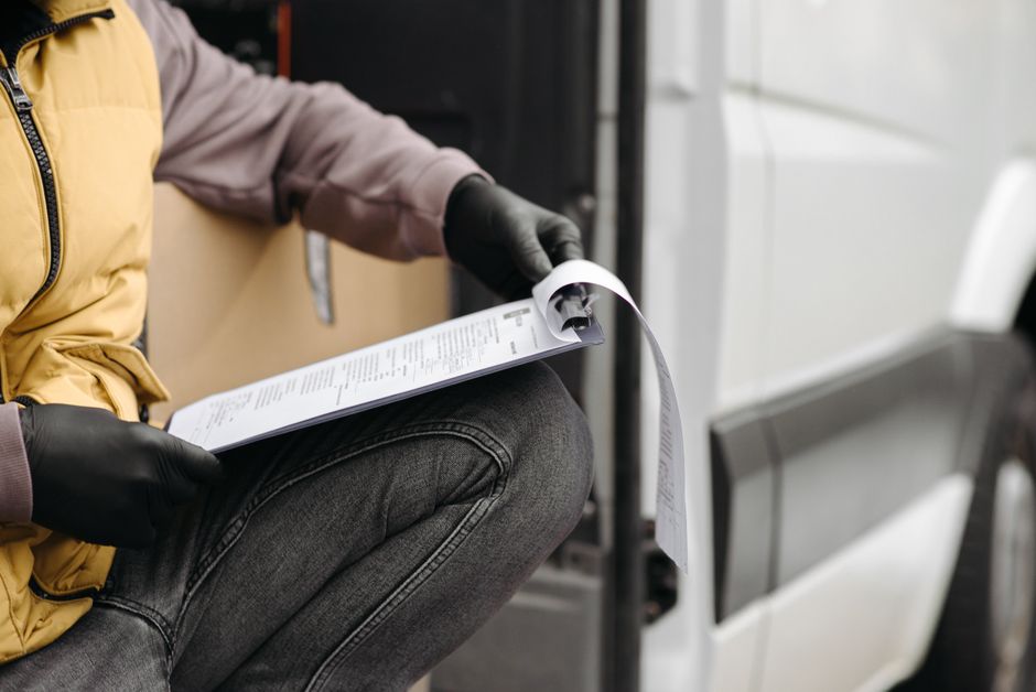 Salaire pendant les vacances : 2 calculs, un piège A delivery worker in gloves checking documents on a clipboard by a van.