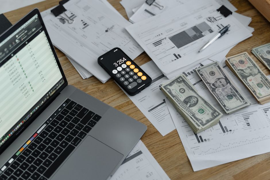 Salaire moyen ou médian : 543 euros d’écart, le piège A desk with financial documents, currency, a laptop, and phone calculator.