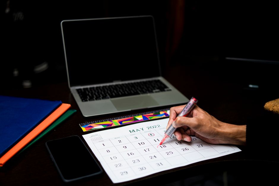 Journée de solidarité : 7 heures sans supplément, le lundi n’a pas toujours le dernier mot A person plans on a calendar at a desk with a laptop and phone, May 2022.