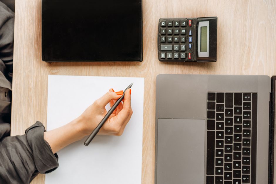 Rupture conventionnelle ou licenciement économique : 4 chiffres avant de signer A person writing on paper surrounded by a laptop, tablet, and calculator on an office desk.