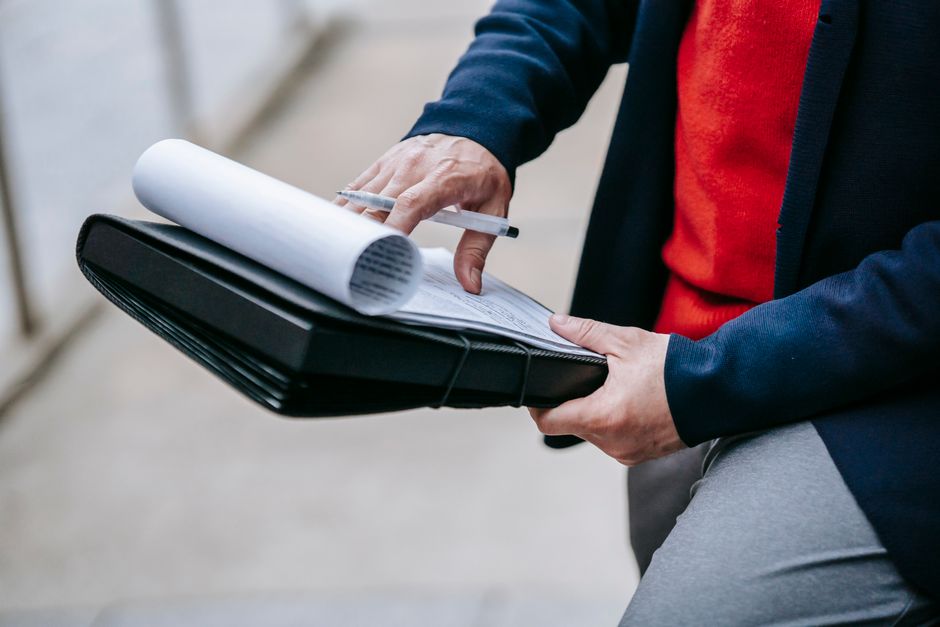 10 certifications pour négocier son salaire, sans badge magique Close-up of a professional person reviewing documents outdoors. Engaged in work with focus on writing materials.