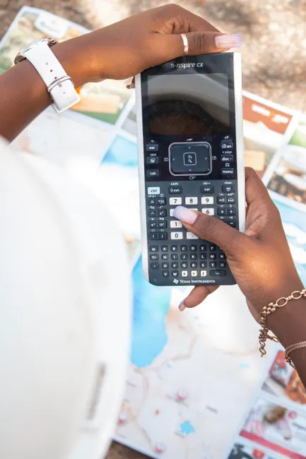 Close-up of hands holding a scientific calculator over a map, creating a dynamic composition.
