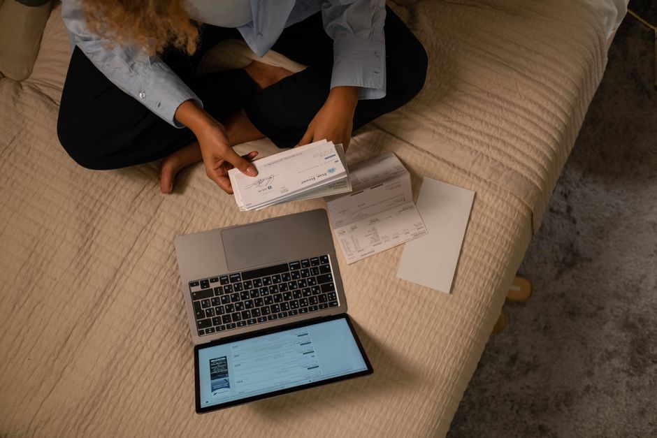 Heures supplémentaires : 220 heures, refus et repos, le vrai calcul Overhead view of woman organizing finances on bed with laptop and checks.