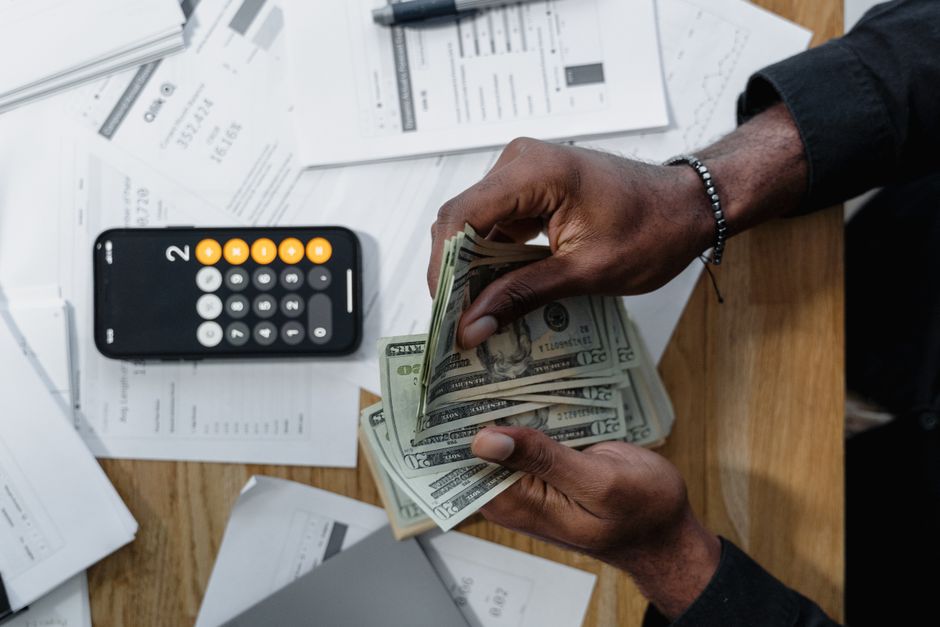 Heures complémentaires à temps partiel : le calcul en 2 paliers Person counting dollar bills over documents with a smartphone calculator on the desk.