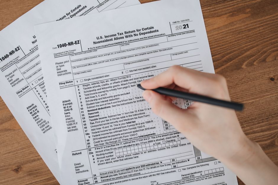 Déclaration de revenus salariés : 7 contrôles à faire Person filling out U.S. tax form 1040-NR-EZ with a pen on a wooden table.