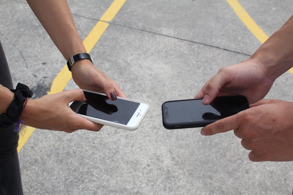 Alternance ou stage : salaire, droits et durée, le vrai calcul Two people exchanging or comparing smartphones in an outdoor setting, focusing on hands and technology.
