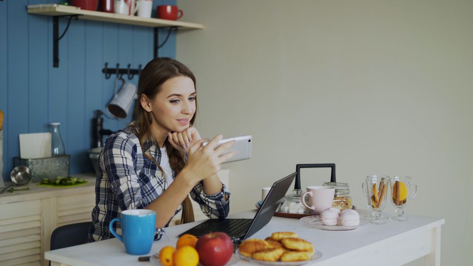 Astreinte au travail : 11 heures de repos et paie à vérifier Young woman using smartphone and laptop while enjoying breakfast in cozy kitchen.